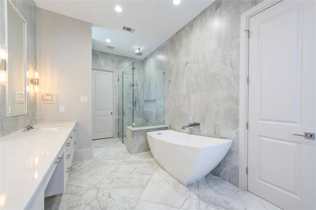 This modern bathroom features elegant marble tiles, a sleek freestanding bathtub, and a spacious glass-enclosed shower. The double vanity offers ample counter space, complemented by contemporary lighting for a luxurious feel.