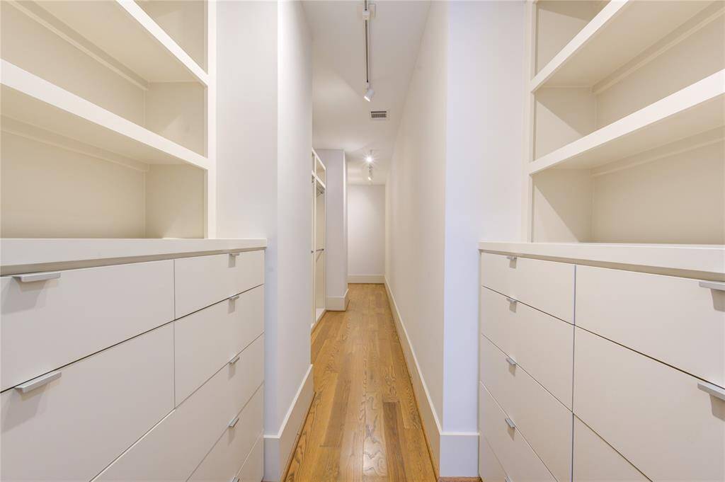 Spacious walk-in closet with ample shelving and storage, featuring sleek white cabinetry and a polished wooden floor, perfect for organizing clothing and accessories.