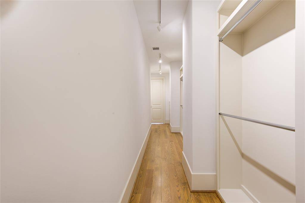 This photo shows a long, narrow walk-in closet with wooden floors and multiple hanging rods, offering ample storage space.
