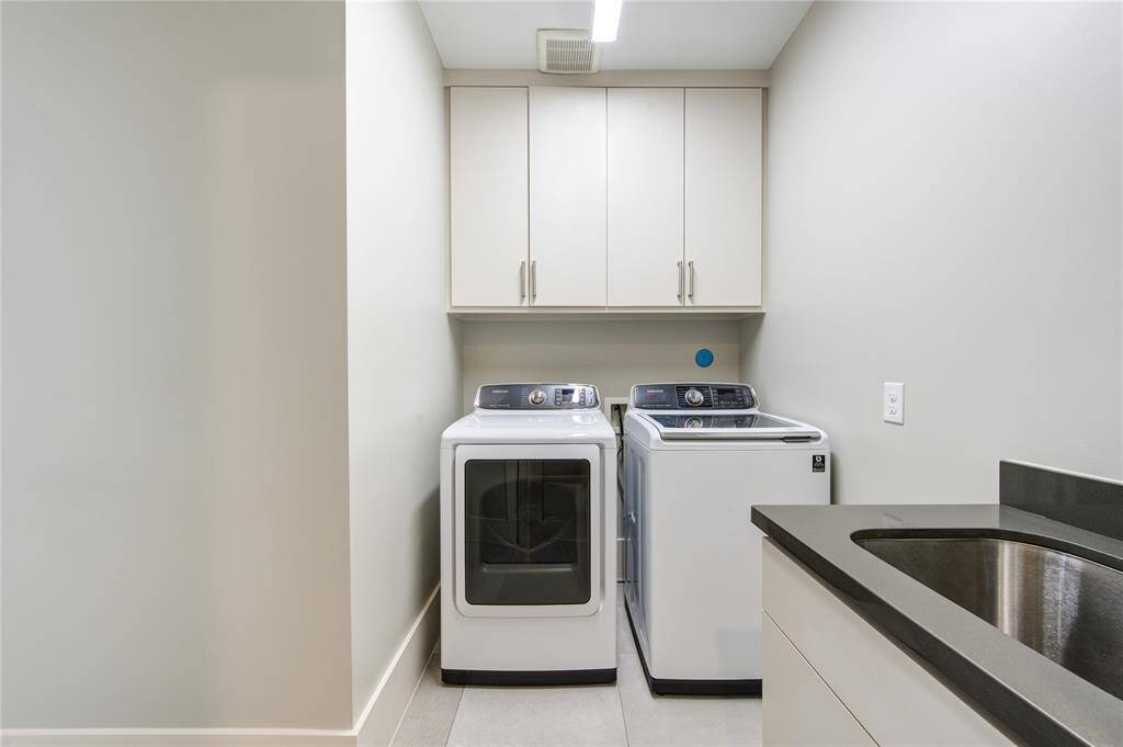 This photo shows a modern laundry room with a washing machine and dryer set, overhead cabinets for storage, and a sleek countertop with a sink.