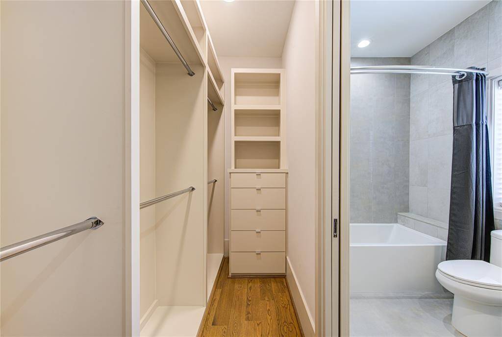 This photo shows a modern bathroom with an adjacent walk-in closet. The closet has ample shelving and hanging space, and the bathroom features a sleek tub with a tiled surround, offering both functionality and style.