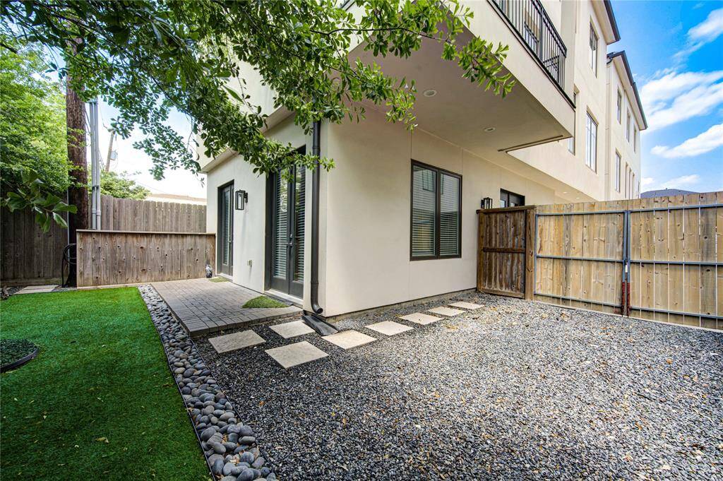 This photo showcases a modern backyard with a mix of artificial grass and gravel, bordered by a wooden fence. The space features a clean, minimalist design with stepping stones and a small patio area. It's ideal for low-maintenance outdoor enjoyment.
