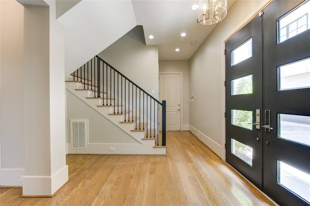 Bright entryway featuring hardwood floors, modern black-framed glass front door, and a sleek staircase with iron railings.