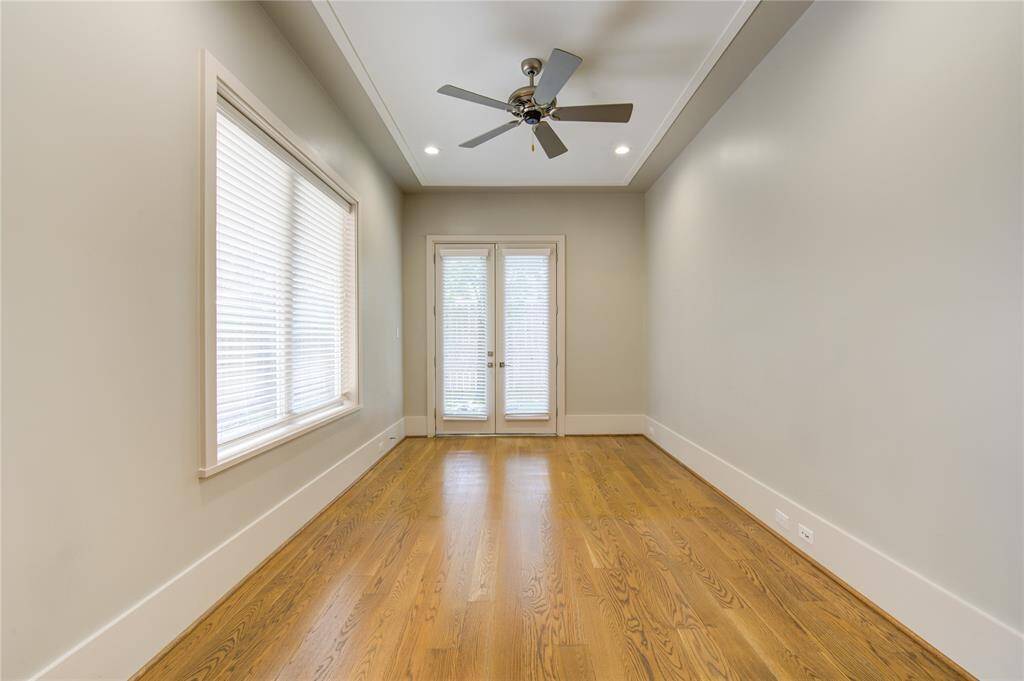 This room features hardwood floors, neutral walls, and a ceiling fan. It has large windows with blinds and a door leading outside, offering plenty of natural light.