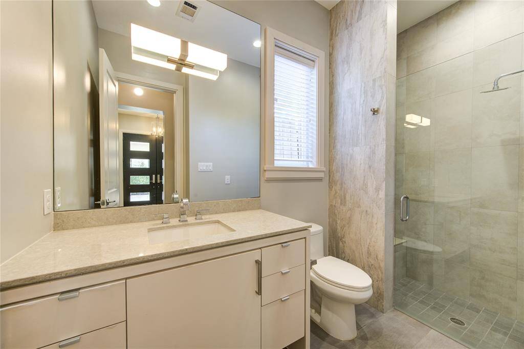 This modern bathroom features a large glass-enclosed shower, sleek vanity with ample storage, and contemporary lighting. Neutral tones and a window provide a bright and inviting atmosphere.