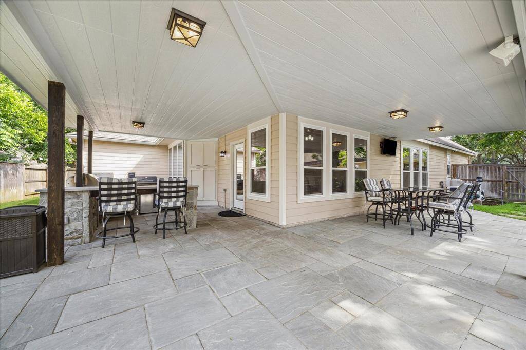 EXPANSIVE NEW PATIO COVER (2025) CREATES A SHADED RETREAT WITH OUTDOOR DINING SPACE, BUILT-IN GRILL AREA, AND STONE BAR.