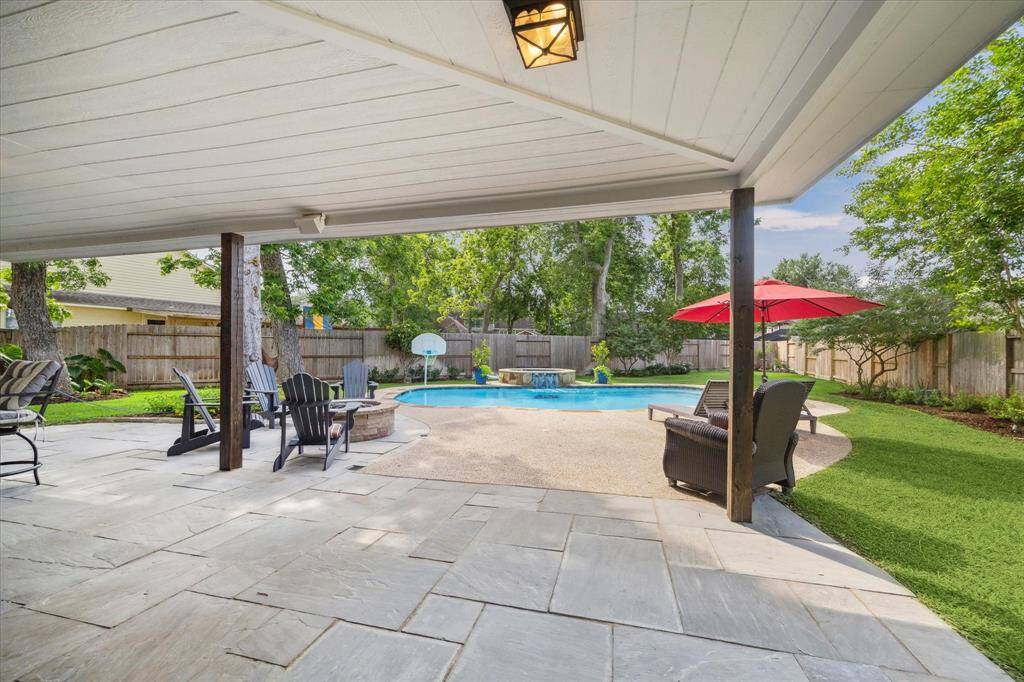 RELAX UNDER THE COVERED PATIO WHILE ENJOYING VIEWS OF THE POOL AND MATURE TREES—A SEAMLESS BLEND OF INDOOR COMFORT AND OUTDOOR LIVING.