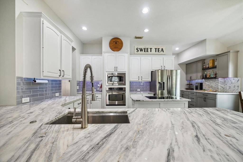KITCHEN FEATURES STUNNING MARBLE COUNTERS, STAINLESS STEEL APPLIANCES & CUSTOM WHITE CABINETRY CREATING A MODERN, FUNCTIONAL SPACE.