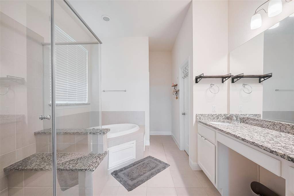 This bathroom features a modern design with a spacious glass-enclosed shower, a separate soaking tub, and dual granite-topped vanities. Bright and airy, it includes ample storage and sleek fixtures, offering a luxurious retreat.