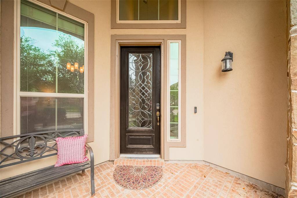 Charming front entry with a decorative glass door, framed by elegant sidelights and a cozy brick patio.