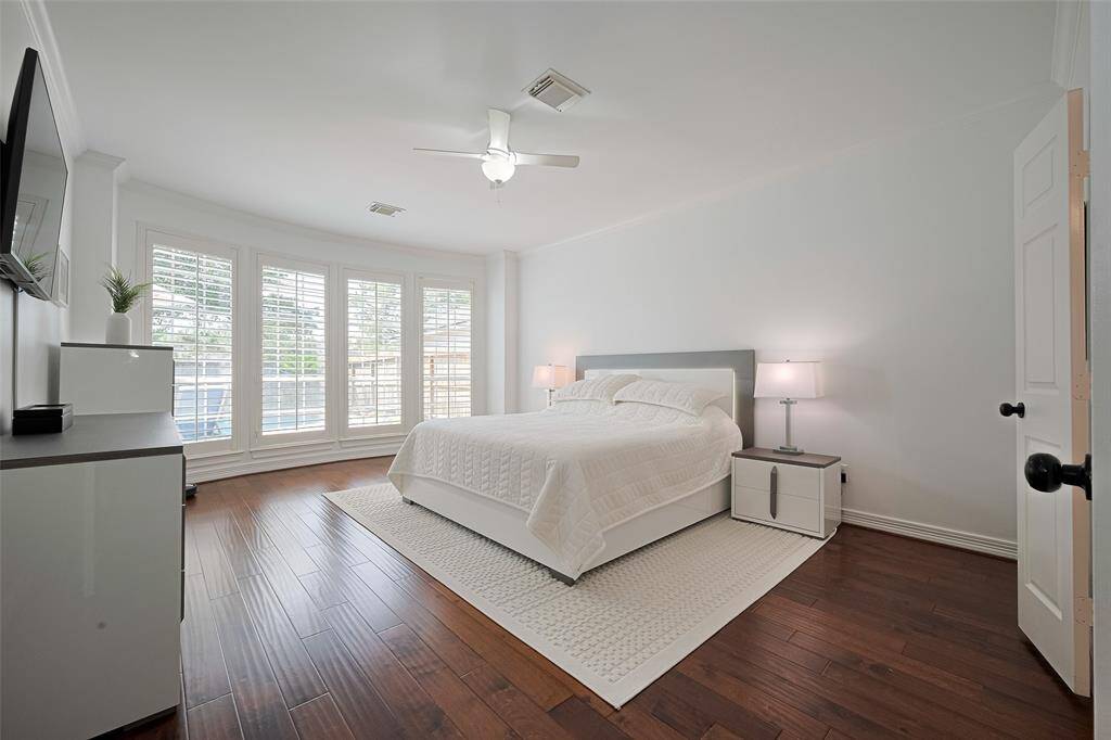 Serenity abounds in this stunning primary bedroom featuring rich wood floors, crisp white paint, modern fixtures and shutters for privacy.