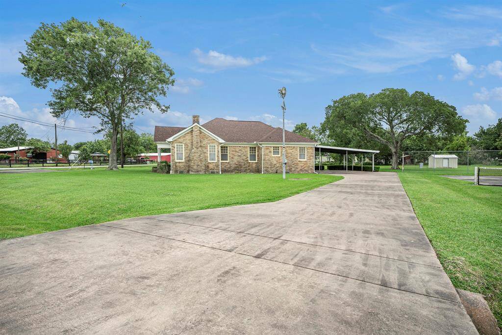 Charming brick home with a spacious driveway and well-maintained lawn. Features a carport and large trees providing shade. Ideal for those seeking a quiet, suburban setting.