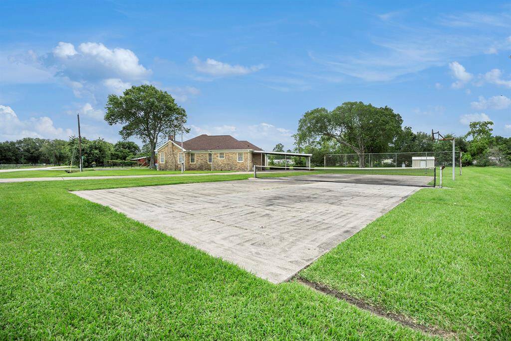This photo showcases a spacious backyard featuring a concrete sports court, lush green grass, and a charming brick house with a covered patio area. It's perfect for outdoor activities and enjoying the serene surroundings.
