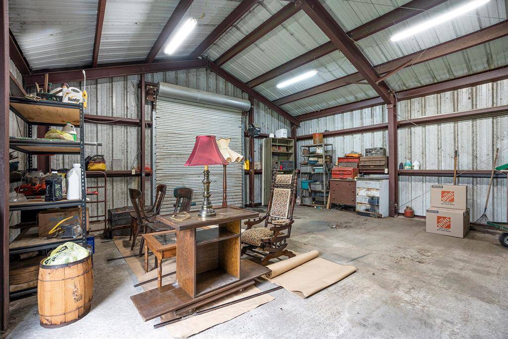 This photo shows a spacious, well-lit metal workshop with high ceilings. It features ample storage with shelves and cabinets, a roll-up door, and concrete flooring, ideal for projects or extra storage space.