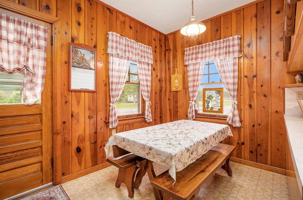 Cozy dining nook with warm wood paneling. The space is illuminated by natural light through windows with charming checkered curtains, creating a welcoming and homey atmosphere.