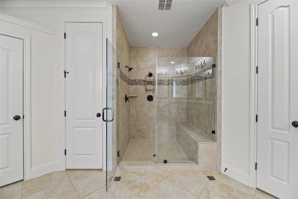 This luxurious primary bathroom shower features dual shower heads for a spa-like experience and a built-in bench for added comfort and convenience. Enclosed by a sleek glass door, the space combines functionality with modern elegance.
