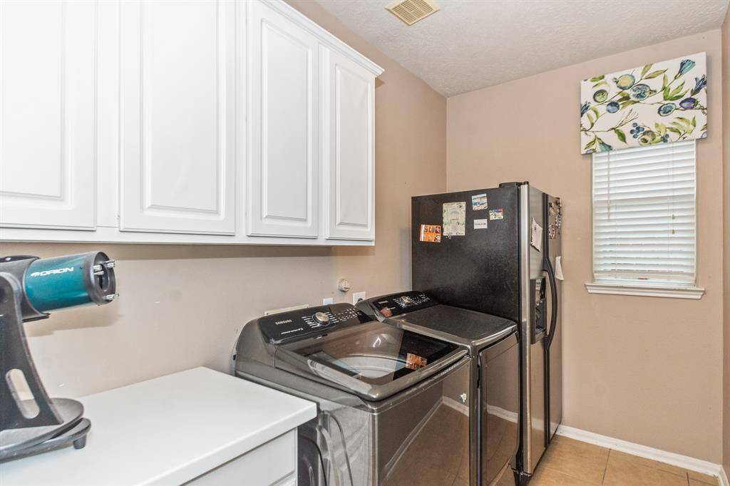 This laundry room features overhead white cabinets for extra storage. A large window provides natural light. The space is neat and functional, perfect for household chores.