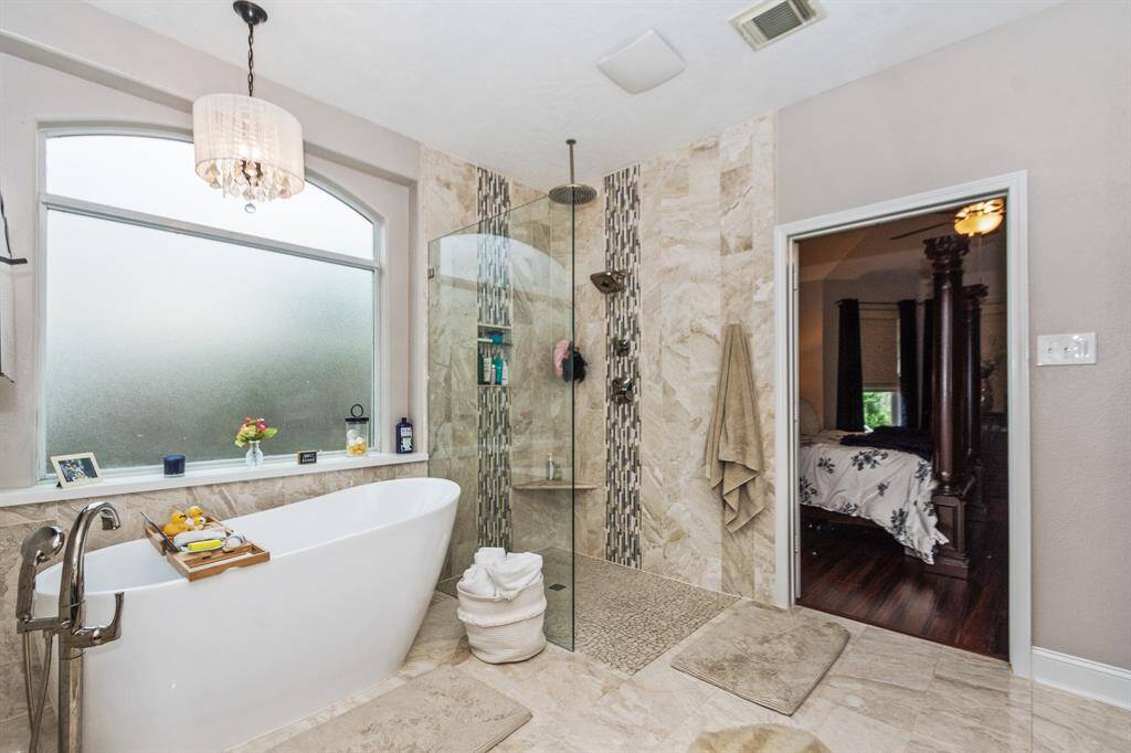 This elegant master bathroom retreat features a freestanding tub, a framless glass shower with modern tiling, and a beautiful chandelier that adds a luxurious touch to your space.