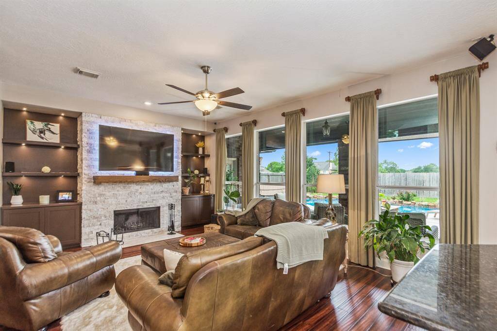 This inviting living room features a cozy fireplace, elegant built-in shelves, and large windows offering a view of the backyard pool.