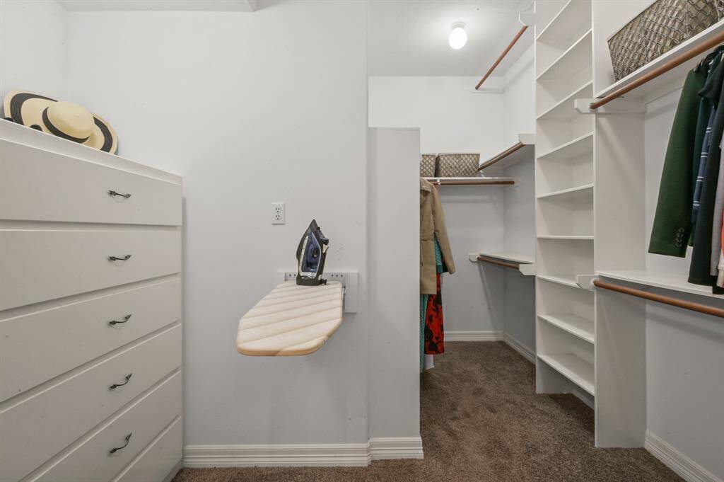 Primary bedroom closet provides built-in dresser, shelving, shoe shelves, collapsable iron board and plenty of hanging space
