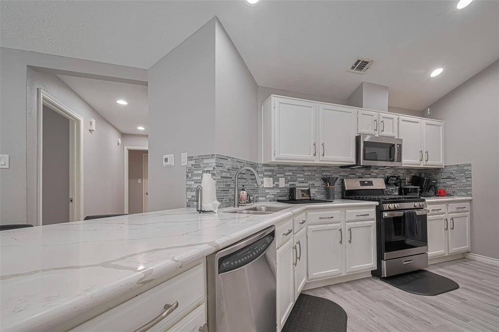 Close up of kitchen quartz counters, updated cabinets, stainless steel appliances and stylish glass tile backsplash