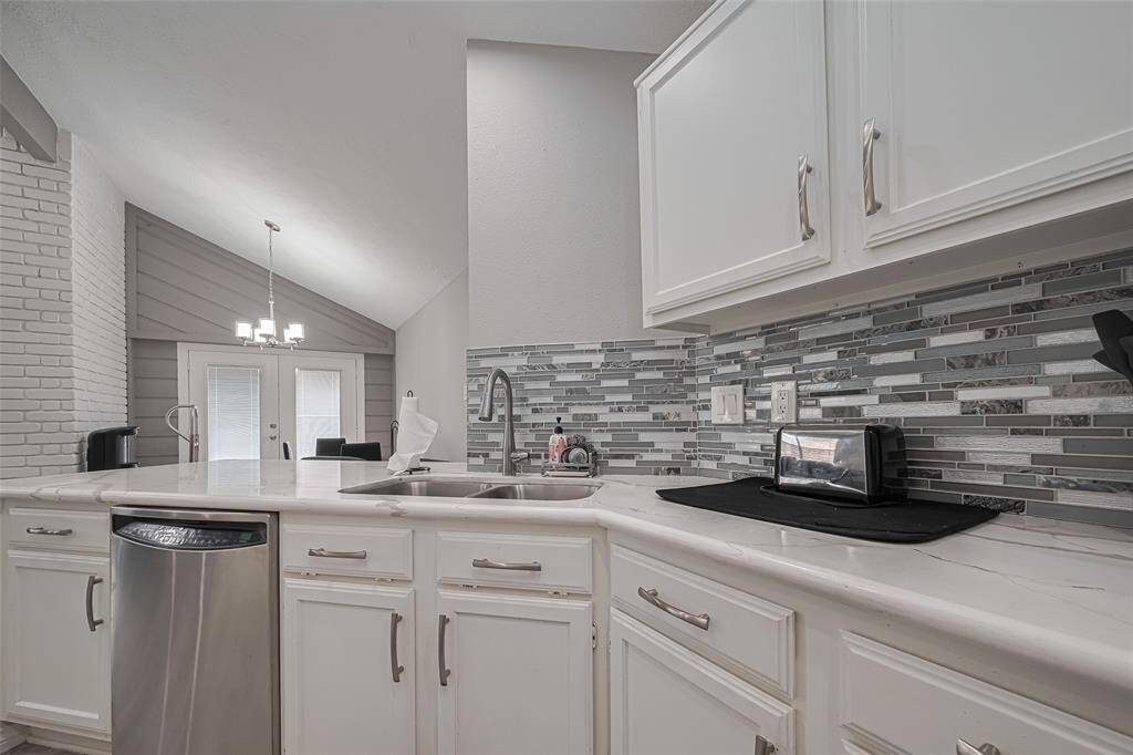 View from kitchen into dining room.  Note: dining room feature wall, contemporary dining room fixture, double dining room doors to patio, brushed nickel gooseneck sink fixture, brushed nickel cabinet hardware, stainless steel dishwasher and glass tile backsplash