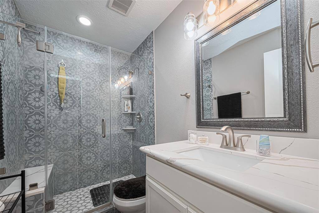 Spacious primary bath showcasing frameless glass shower w/marble floor, bench seating, designer tile, quartz counter, undercounter sink and recent fixtures & hardware