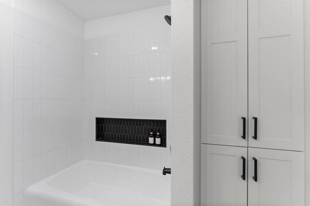 New modern tub/shower in crisp bright white tile, shelf in contrasting black tile adds a designer feature, and  custom built-in cabinets have ample storage space.