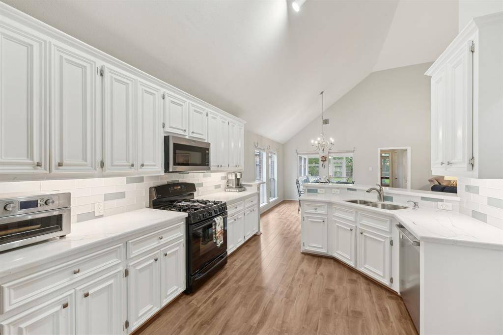 Modern kitchen with gas stove, double sink, quartz countertops, white cabinetry and subway tile back splash.