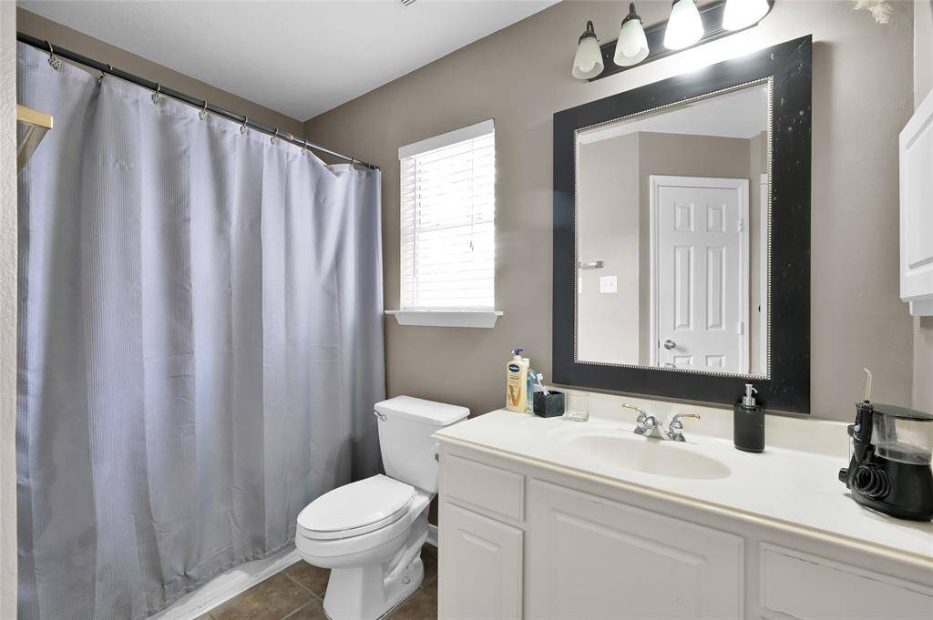 This is a bright bathroom, a toilet, and a white vanity with a large mirror. The walls are painted in a neutral tone, and  a window providing natural light.
