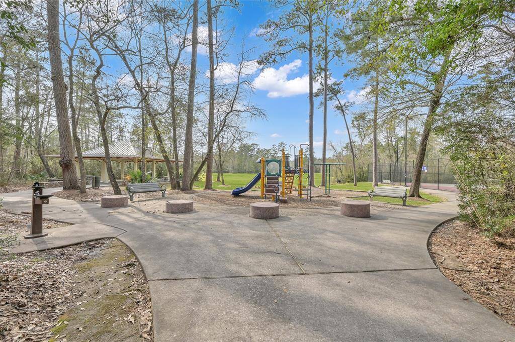 A serene park area with a playground, benches, and a covered pavilion surrounded by trees.