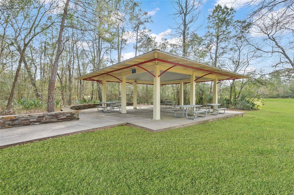 Outdoor pavilion set in a lush, wooded area, featuring picnic tables and a well-maintained grassy lawn, perfect for gatherings and relaxation.