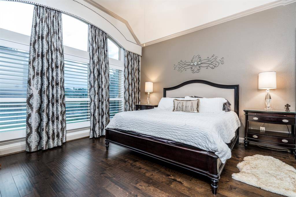 Primary bedroom with black out custom designed hotel type curtains, wood flooring, ceiling fan, and crown molding. You have a view of the lake and fountain from the bed!