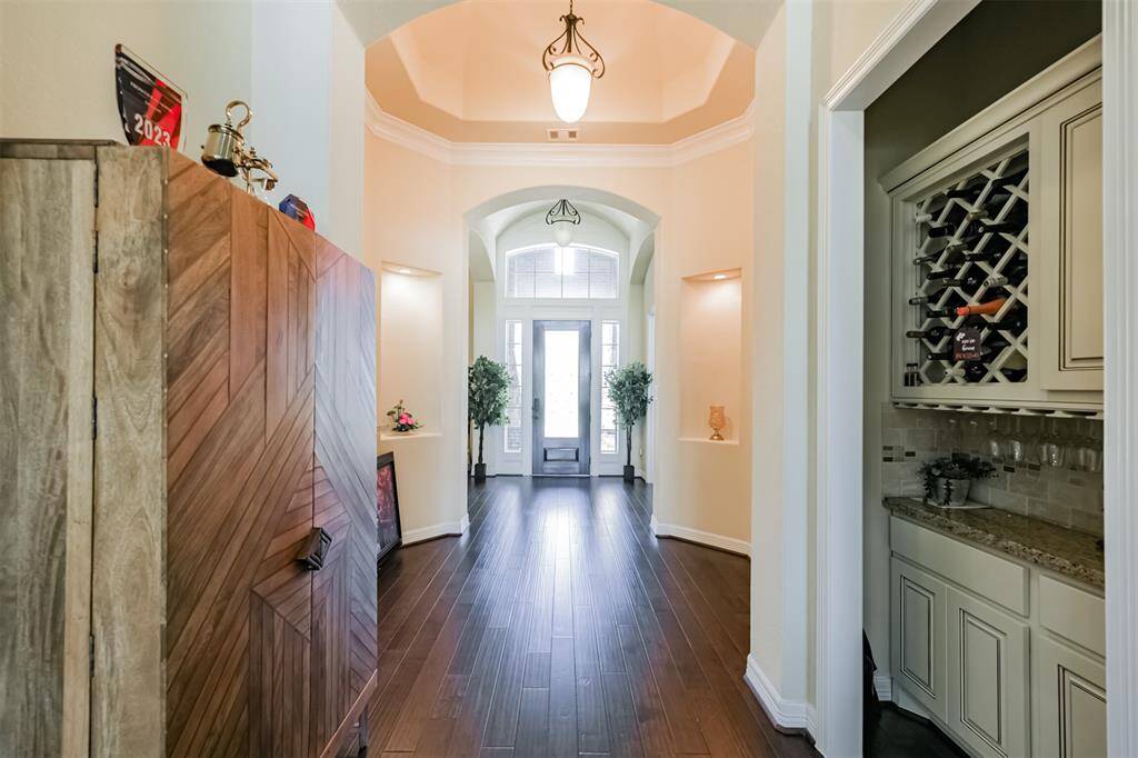 This photo highlights the Entry, the  Foyer with art niches, hardwoods, and the Wine Bar. Notice the architectural styling featuring arched walkways, hexagon tray ceiling and floor, crown molding and the openness of this floor plan.