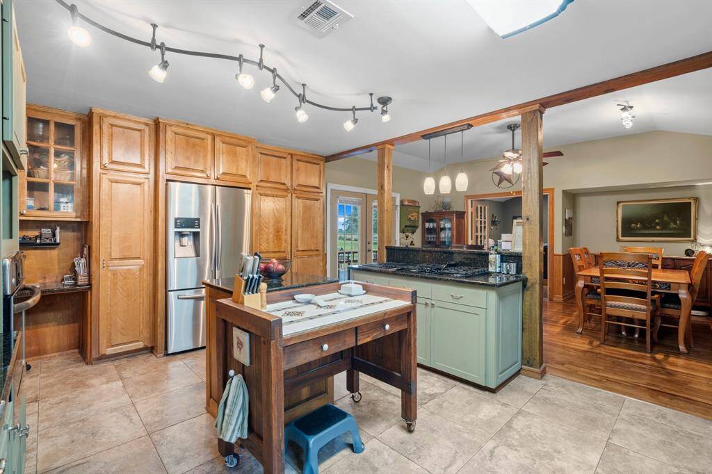 Tasteful mixture of painted and natural wooden cabinetry, stainless steel appliances, and a central island with granite countertops. The open layout connects seamlessly to the cozy dining area.