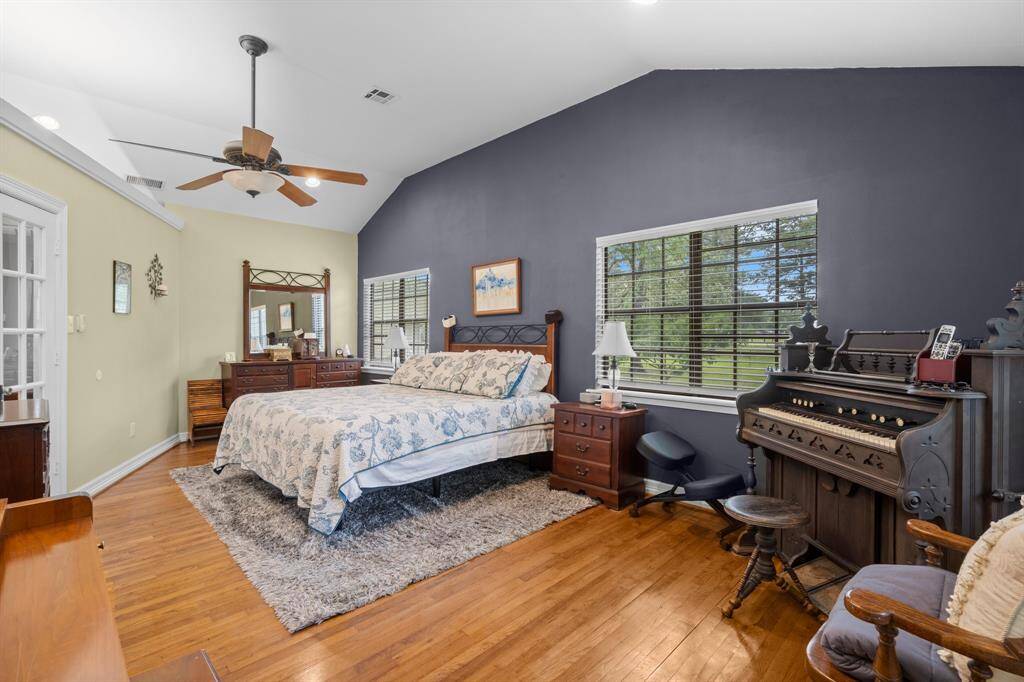The spacious primary bedroom features a vaulted ceiling with a fan, hardwood floors, and a large window offering plenty of natural light.