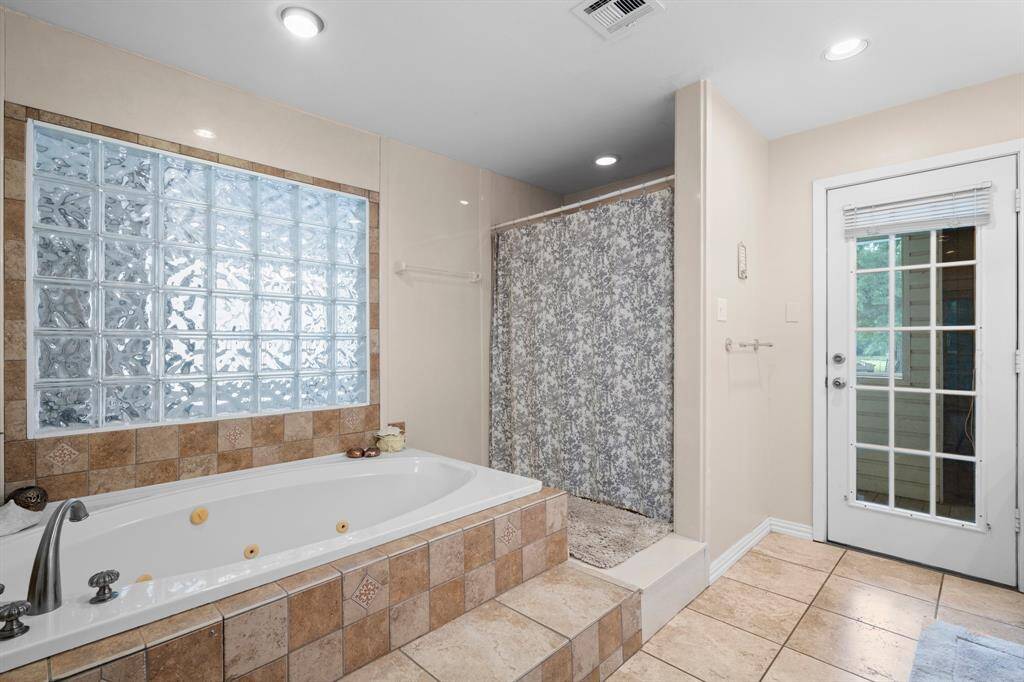 This bathroom features a spacious, tiled soaking tub with a glass block window. The space is well-lit with recessed lighting and has neutral tile flooring.