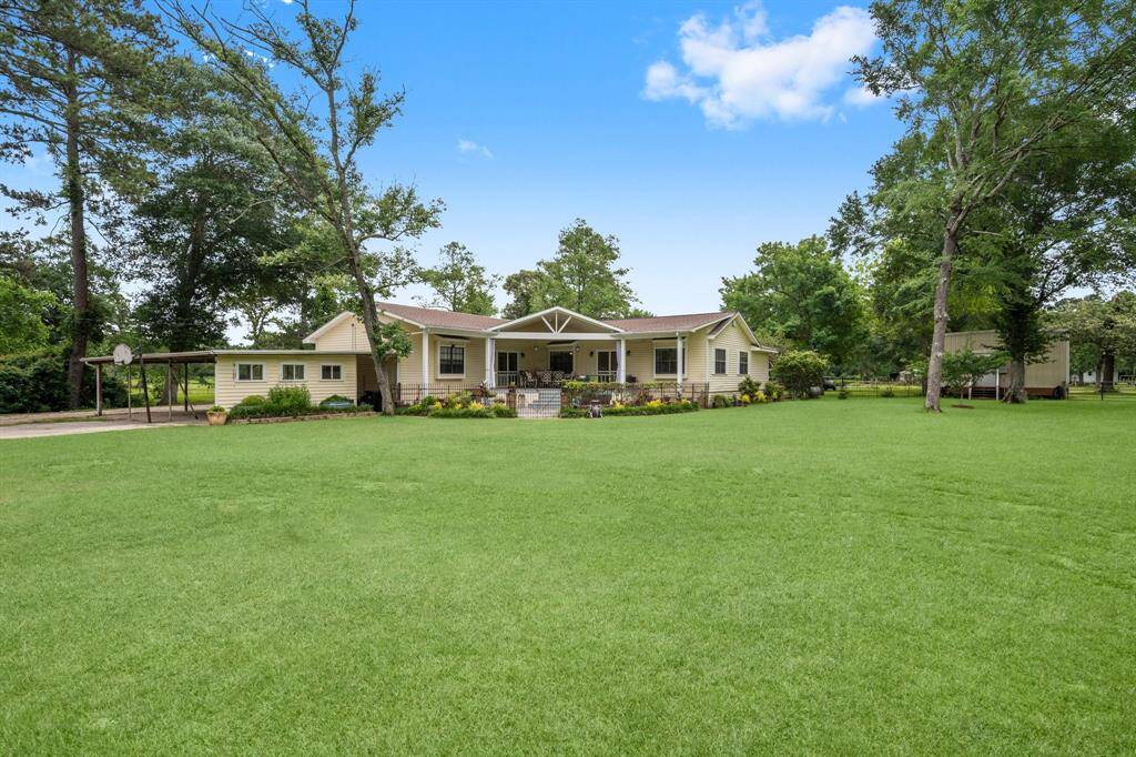 This charming home features a spacious front yard with lush green grass and mature trees. The house has a welcoming porch and a covered carport.