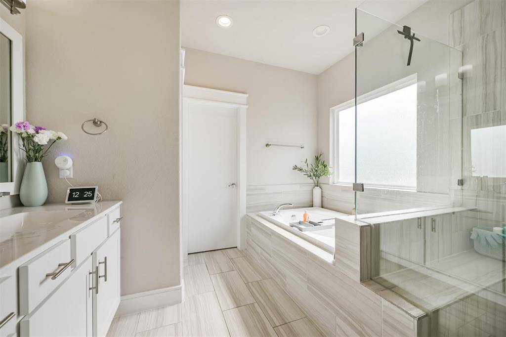 An oversized walk-in frameless shower includes a bench and plenty of space for personal items, and a separate soaking tub. The space is well-lit and includes a frosted window for privacy.
