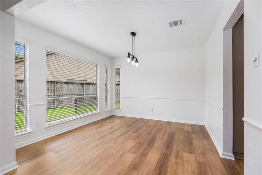Bright and airy dining room with large windows offering plenty of natural light, featuring luxury vinyl flooring and a new modern light fixture.