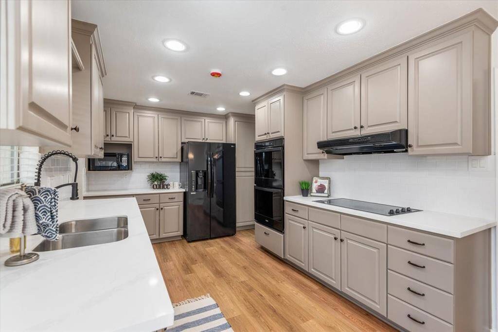 This kitchen features modern cabinetry, sleek black appliances, and ample counter space. It has recessed lighting, a double sink, and luxury vinyl flooring, creating a warm and functional cooking area.