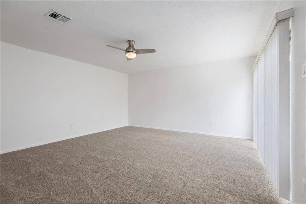 This spacious primary bedroom features new carpet, new ceiling fan, and ample natural light from large sliding glass doors for ease into the backyard.