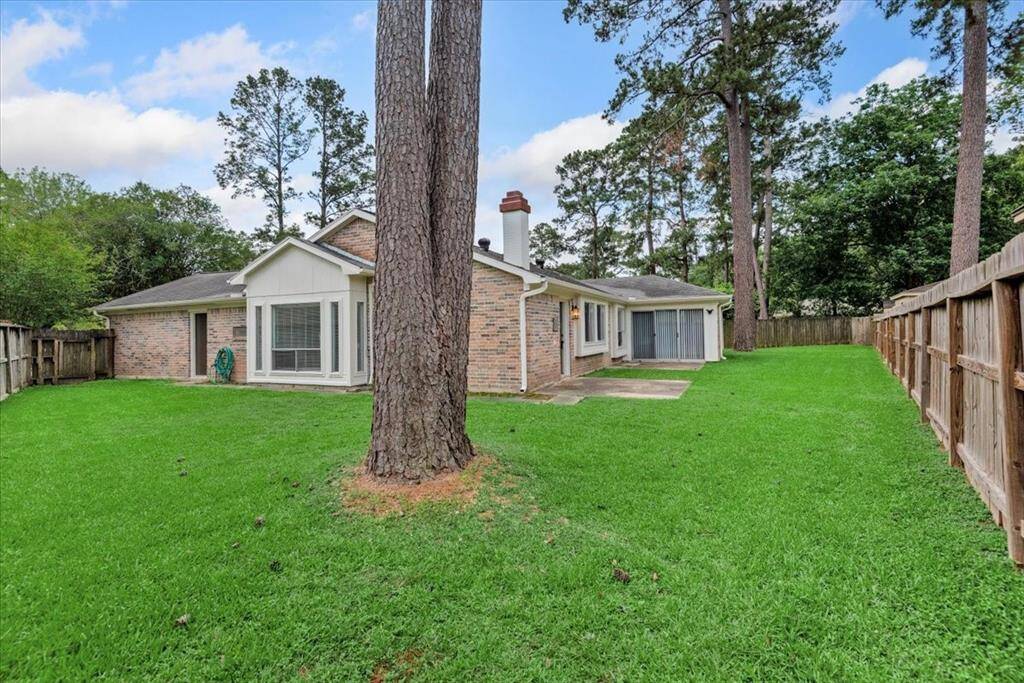 This photo showcases a single-story brick home with a spacious, fenced backyard. The yard features tall trees, providing natural shade, and a well-maintained lawn. The house includes large windows and a sliding glass door, enhancing natural light and outdoor access.