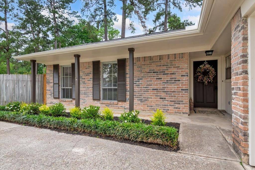 Charming single-story home with a brick exterior and covered front porch. Features a welcoming front door adorned with a wreath, and a neatly landscaped front yard with mature trees in the background. Ideal for those seeking a cozy and inviting space.