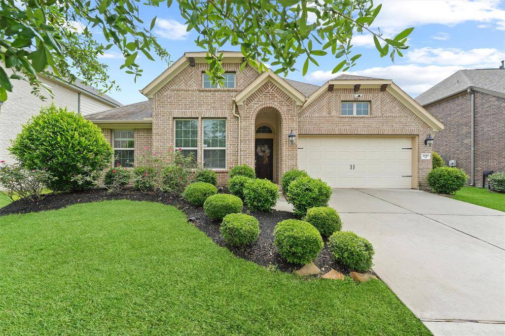 This charming brick home features a well-maintained front yard with lush greenery and neatly trimmed bushes. It has an inviting arched entryway and a spacious three-car garage, offering great curb appeal.