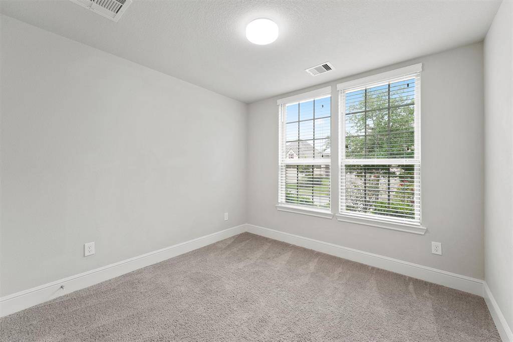 Bright, cozy room with light gray walls and plush carpet. Features a large window with blinds, offering ample natural light and a view of greenery. Perfect for a bedroom or home office.
