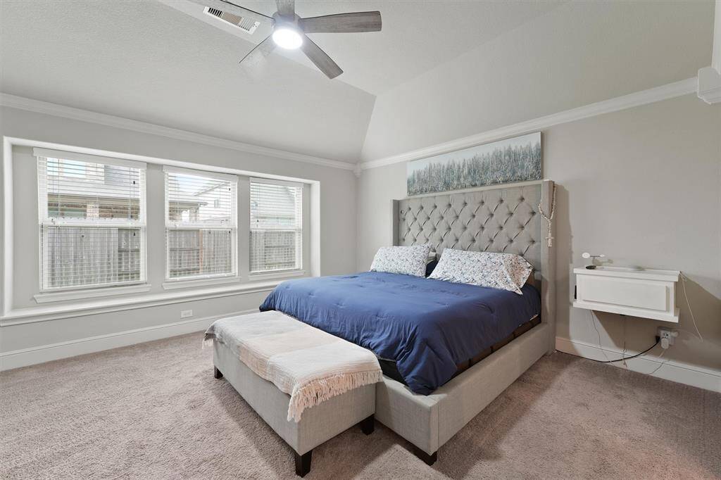 This spacious bedroom features a plush carpeted floor, large windows for natural light, a stylish tufted headboard, and a ceiling fan. Ideal for relaxation and comfort.