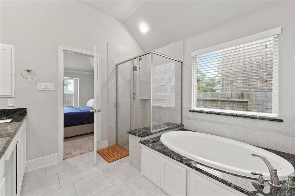 This bathroom features a sleek design with a large soaking tub, a glass-enclosed shower, and dual sinks with granite countertops. Natural light enters through a sizable window, creating a bright and inviting space.