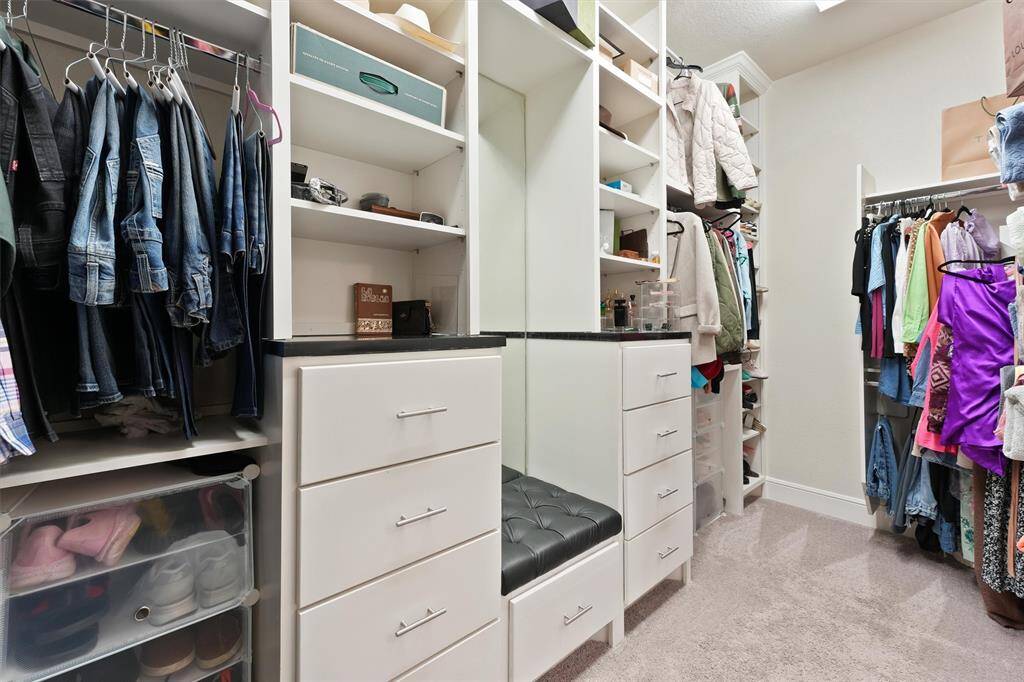 This spacious walk-in closet features ample hanging space, open shelving, and multiple drawers for organized storage. It includes a built-in bench with a cushioned seat, perfect for convenience and comfort.