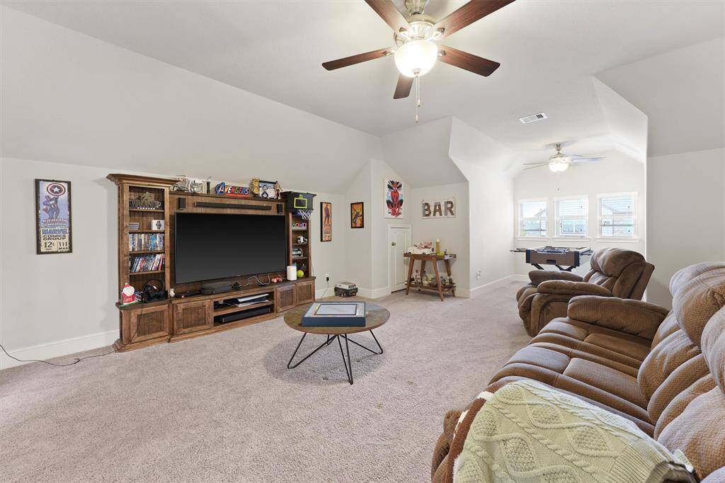 Spacious entertainment room with plush seating, large TV, and game area. Features a cozy bar nook and natural light from multiple windows, perfect for relaxing or hosting.